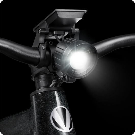 Velotric - Summit 1 handlebars with a mounted bike light turned on, shining brightly against a dark background.
