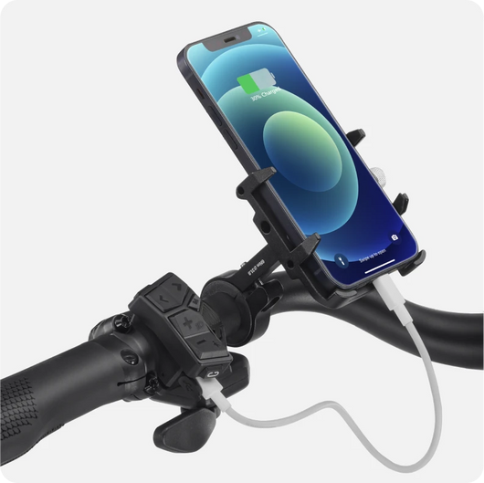 A smartphone mounted on a Velotric Discover 1 bike handlebar, connected to a charging cable. The phone screen shows a charging icon.