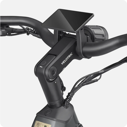 Close-up of an electric bike handlebar featuring a Velotric - Discover 1 display screen mounted at the center, surrounded by wires. Explore this model at Tampa Bay eBikes for a seamless riding experience.