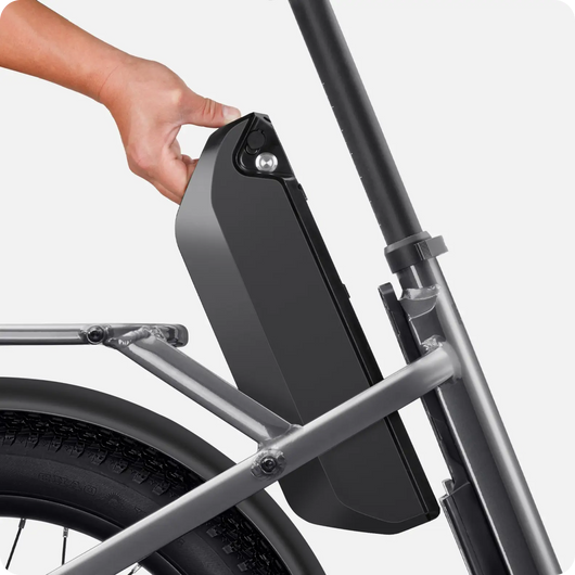 A hand removing the battery pack from a Velotric Fold 1 electric bicycle. The battery is mounted on the frame behind the front wheel.