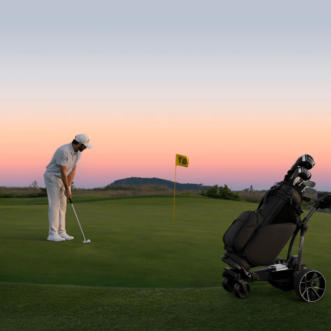 A golfer in white putts on a green at sunset near Tampa Bay golf, with a yellow “18” flag and a Navee Birdie 3X electric push cart by Navee in the foreground.