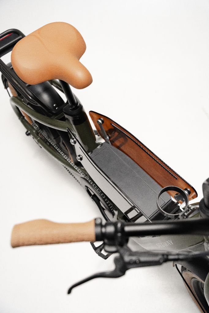 Top-down view of the Segway Muxi electric utility bike by Segway, featuring a tan seat and handlebar grips, black frame and chain, plus a brown transparent protective side panel on its central cargo area.