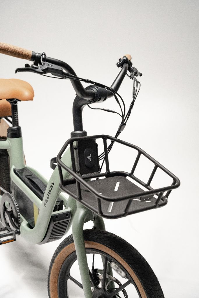 A close-up of the Segway Muxi by Segway shows its front section with a black metal basket on the handlebars and matching tan seat and grips.