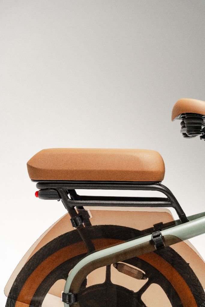 Close-up of the Segway Muxi electric utility bike’s rear section, showing its tan seat, rear rack, and part of the wheel against a plain background.