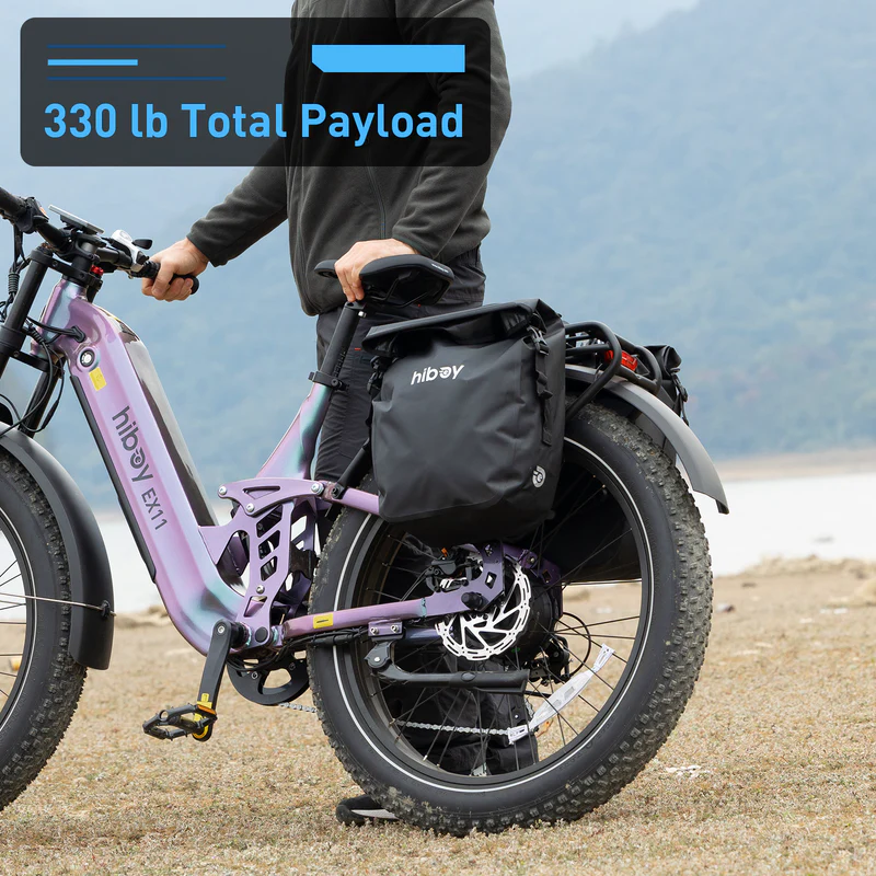 A person stands by a Hiboy - EX11 full suspension electric bike with large tires and a black side bag, outdoors near water. Text: "330 lb Total Payload.