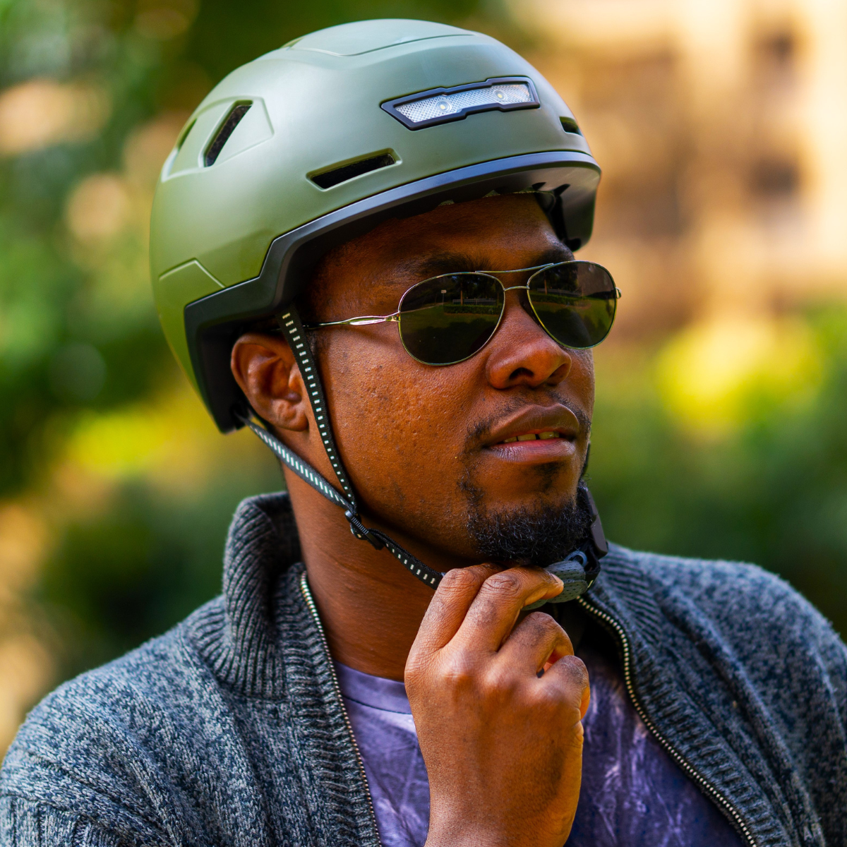 A man wearing sunglasses and a XNITO e-bike helmet is fastening the helmet strap under his chin.