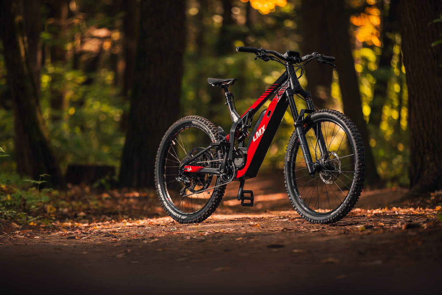 A red and black LMX - 64 electric mountain bike with a brushless mid-mounted motor is parked on a dirt trail in a forest, sunlight filtering through the trees. With pedal assistance from LMX, this ride promises both power and efficiency for any adventure.