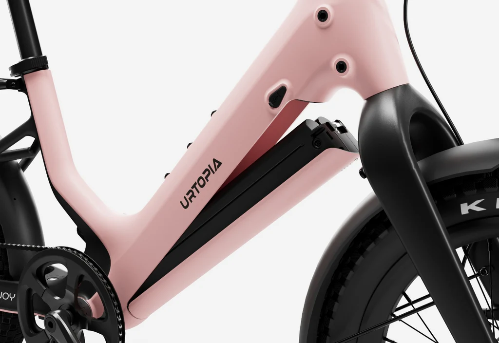Close-up view of the Urtopia Carbon Joy Ultra e-bike frame in pink, showing the battery compartment along with part of the front wheel and pedal system.