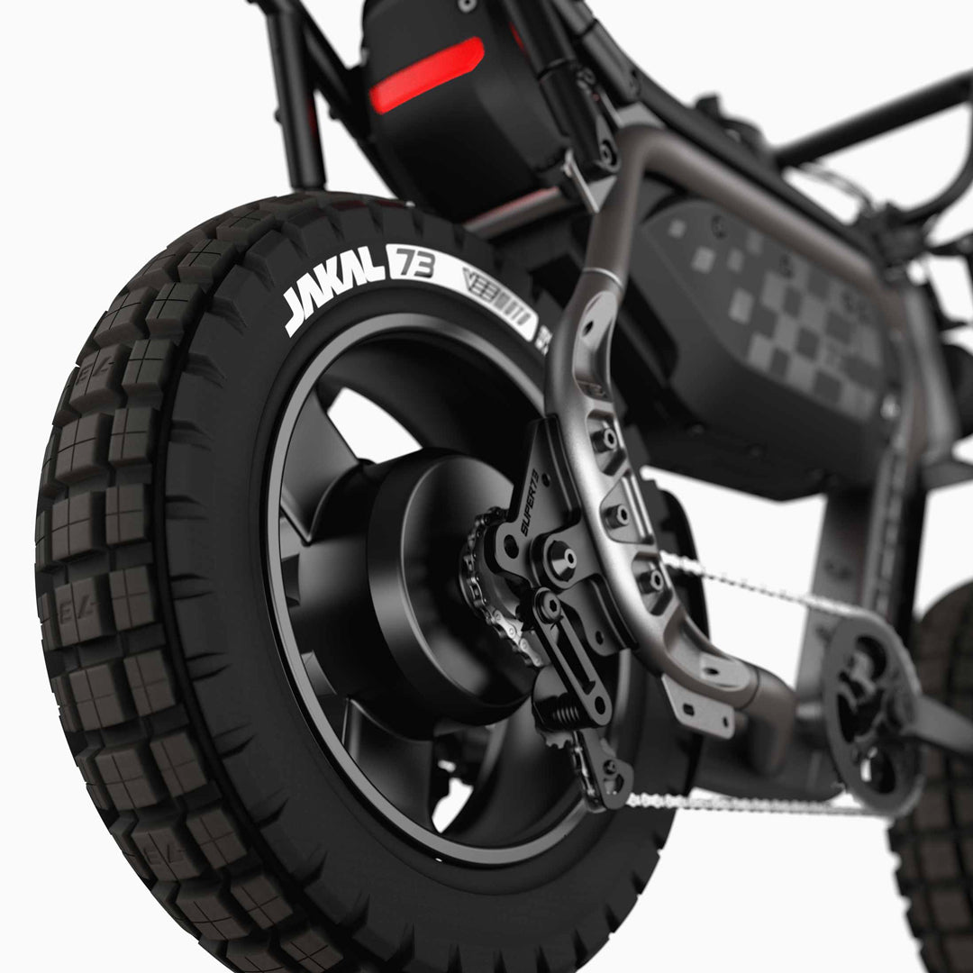 Close-up of the rear wheel and suspension on the Super 73 - MZFT eBike by Super 73, highlighting the tire tread, chain, disc brake, and a section of the branded frame.