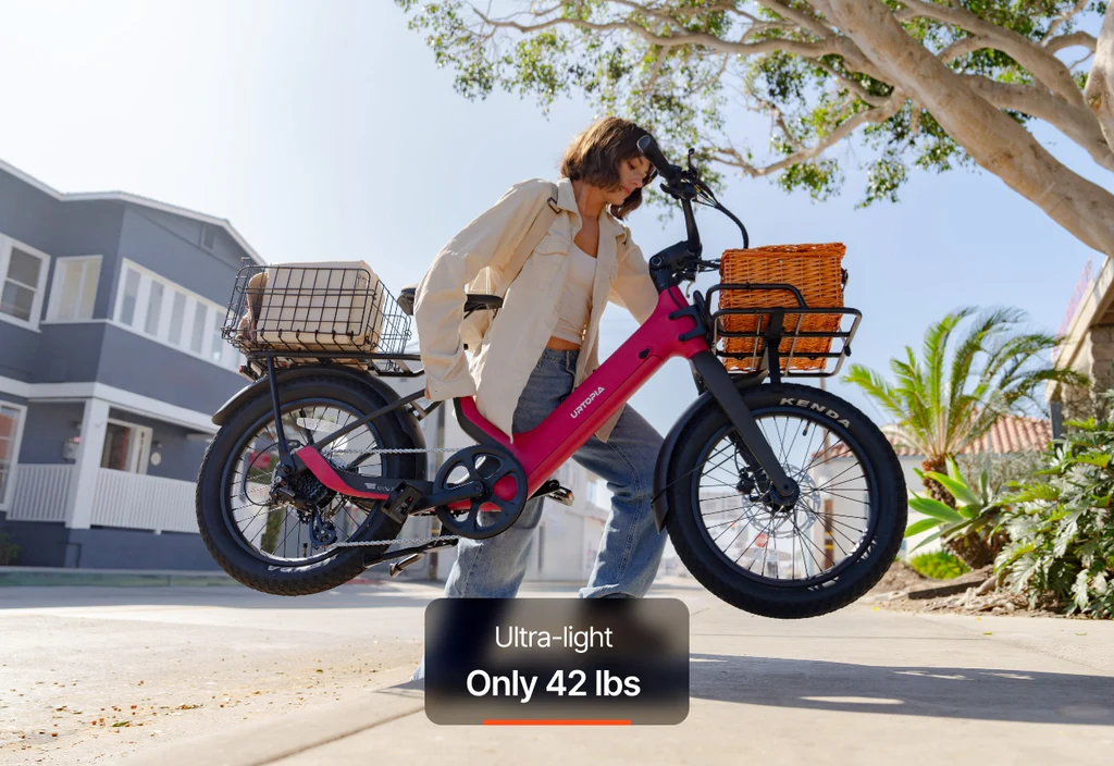 A person lifts a Urtopia - Carbon Joy Ultra electric cruiser bike with baskets in front of a house; text overlay reads "Ultra-light Only 42 lbs. Long-range battery for extended rides.