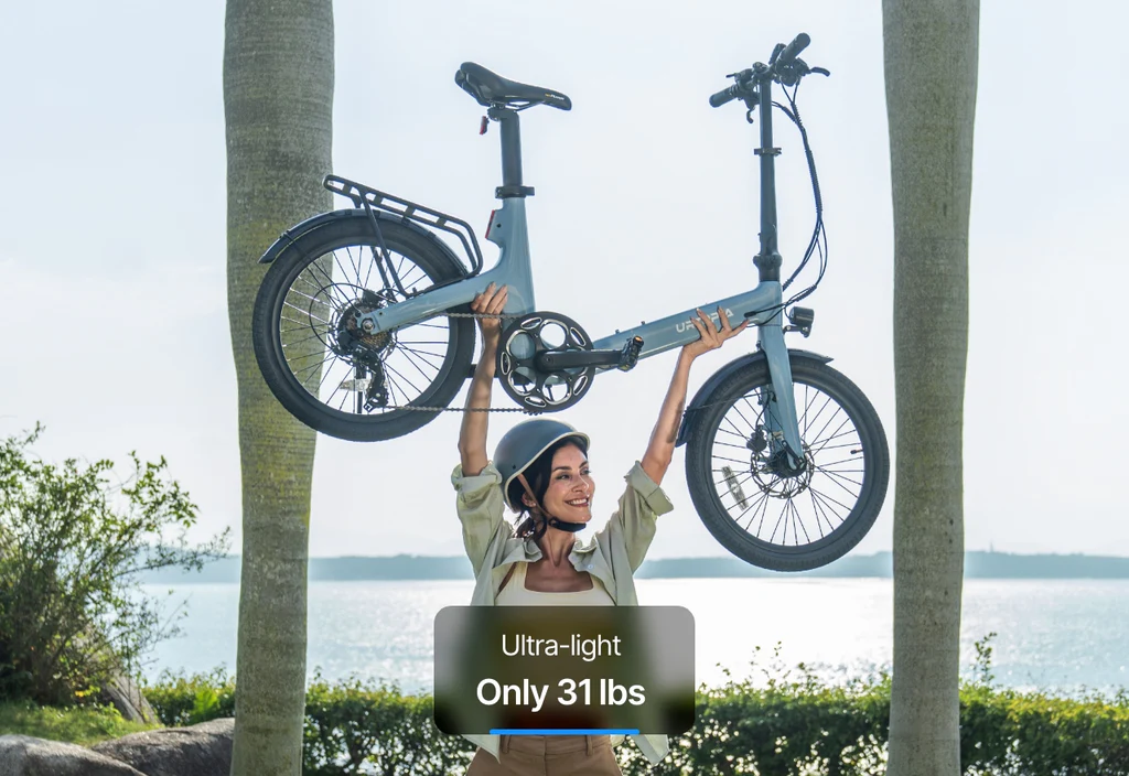 A woman in a helmet lifts the Urtopia Carbon Fold Step-Thru e-bike (by Urtopia), weighing just 31 lbs, above her head at the beach. Text reads: "Ultra-light Only 31 lbs.