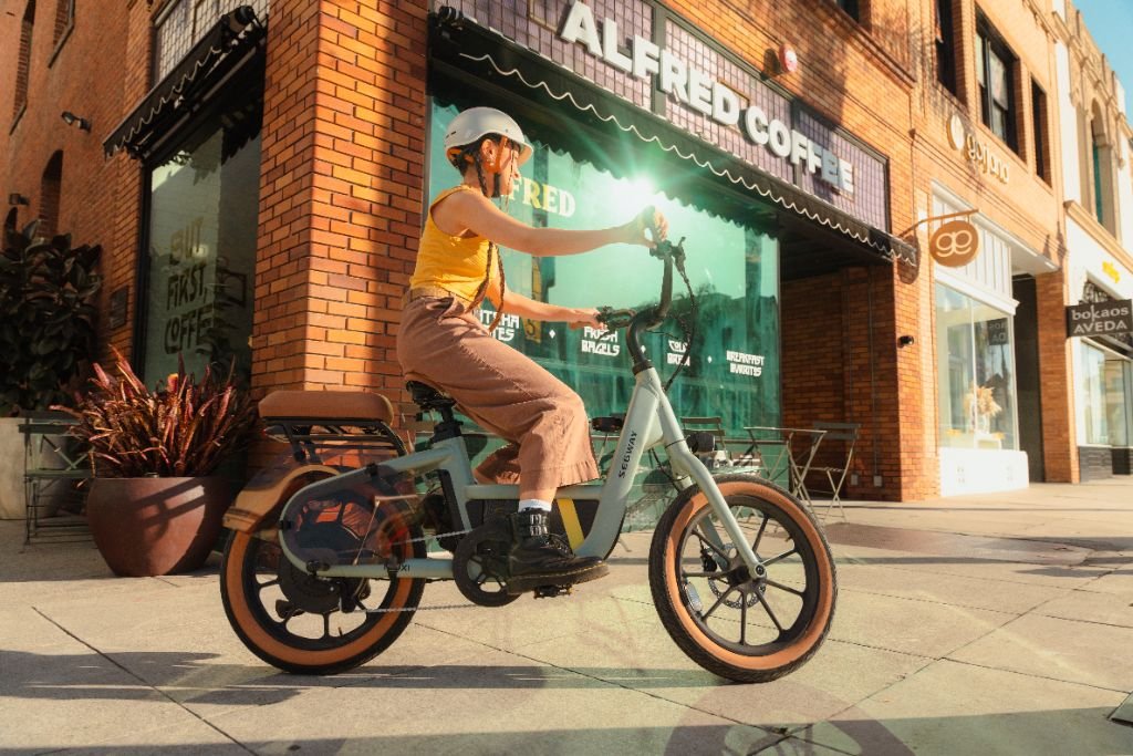 A person in a helmet and casual clothes sits on a Segway Muxi electric utility bike with a 750W motor, parked outside Alfred Coffee.