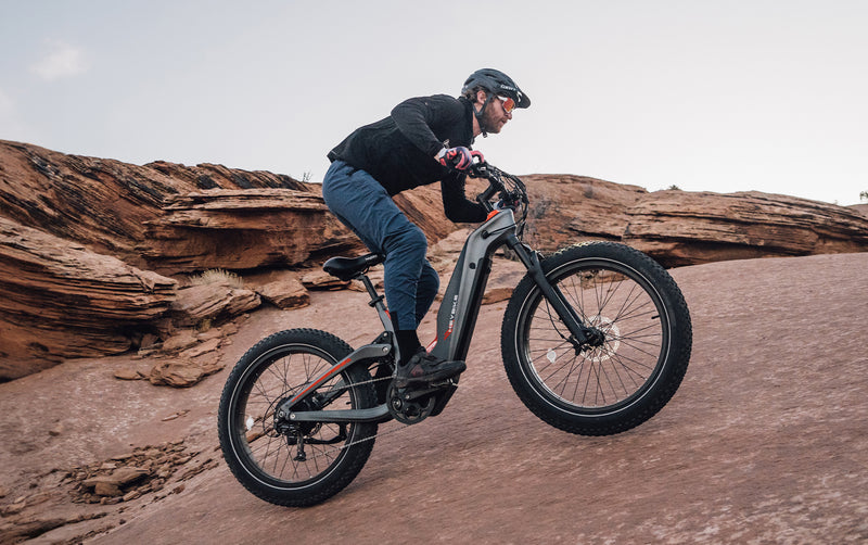 A person mountain biking up a steep, rocky slope, focusing intently as they maneuver their HeyBike - Hero (Mid-Drive).