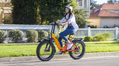 Woman wearing a helmet rides a colorful HeyBike - Horizon electric bike with fat tires on a suburban street, smiling.