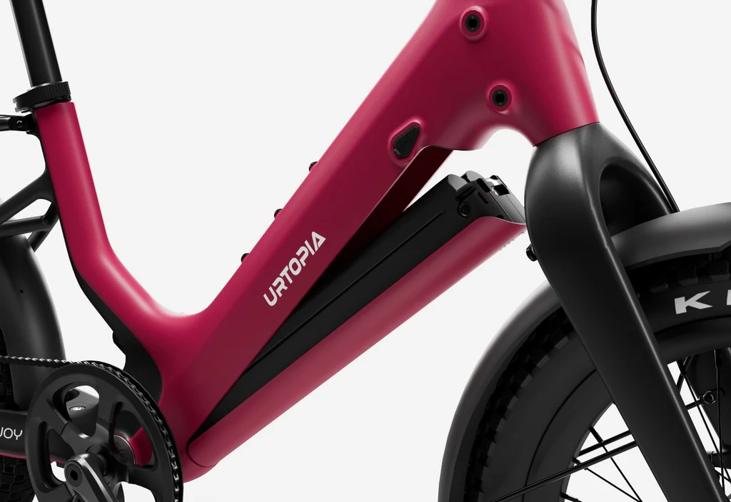 Close-up of the Urtopia - Carbon Joy Ultra carbon fiber e-bike frame in red, featuring an integrated battery, with part of the front wheel and pedal visible.