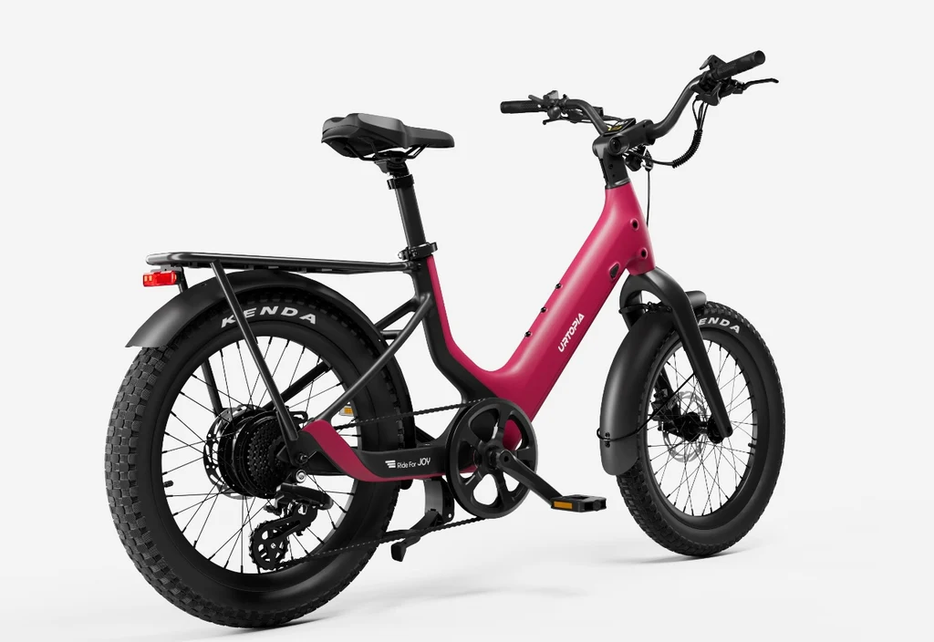 The Urtopia Carbon Joy Ultra by Urtopia, a matte pink electric cruiser bike with thick tires, rear rack, and front and rear fenders, is shown from a rear-side angle on a plain white background.