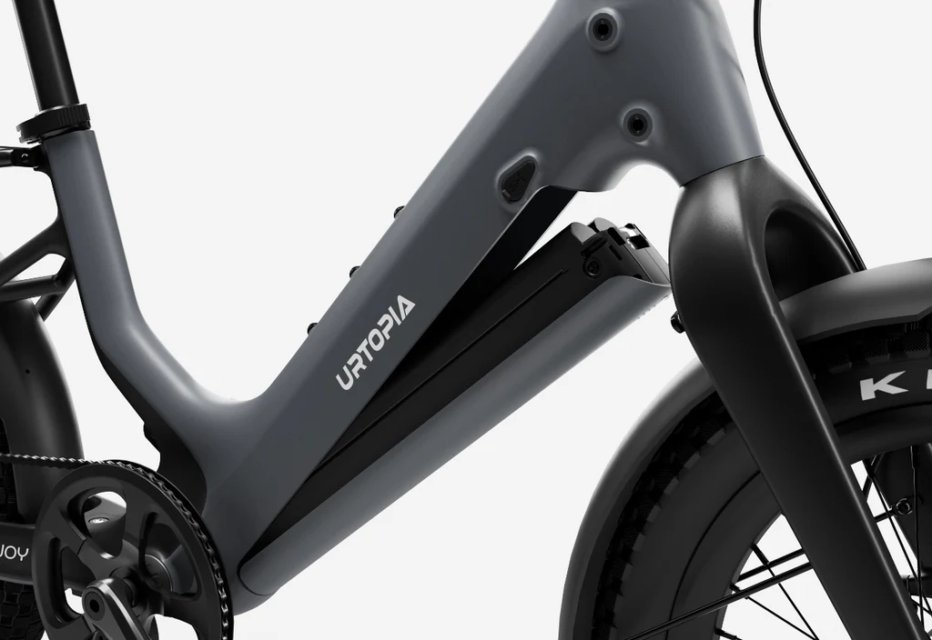 Close-up view of the Urtopia Carbon Joy Ultra e-bike’s matte grey carbon fiber frame, featuring "Urtopia" branding, integrated battery, and part of the front wheel.