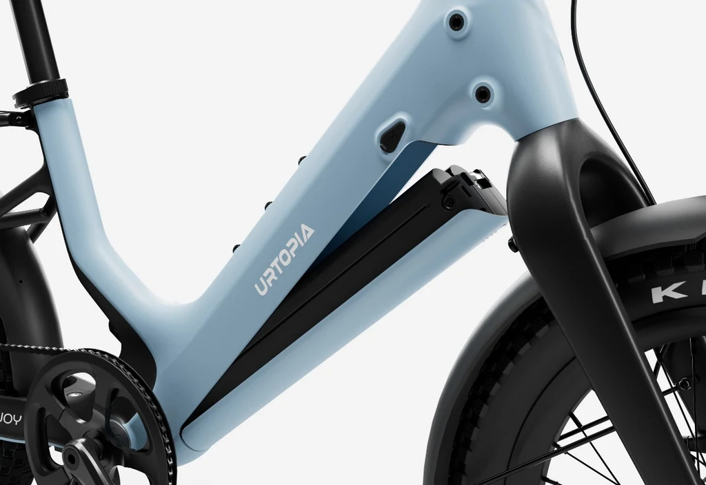 A close-up of the Urtopia - Carbon Joy Ultra e-bike by Urtopia, showcasing its light blue carbon fiber frame, battery compartment, and partial front wheel with crankset.