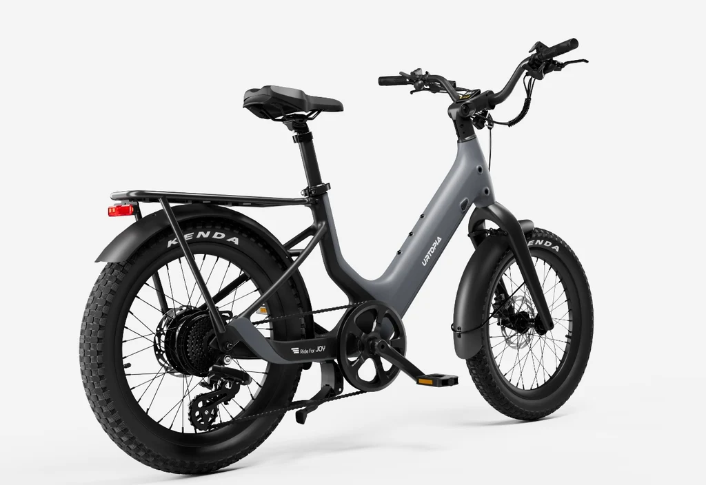 The Urtopia Carbon Joy Ultra by Urtopia is a matte gray long-range e-bike with a step-through frame, rear cargo rack, wide Kenda tires, and black fenders, shown from a rear-side angle.