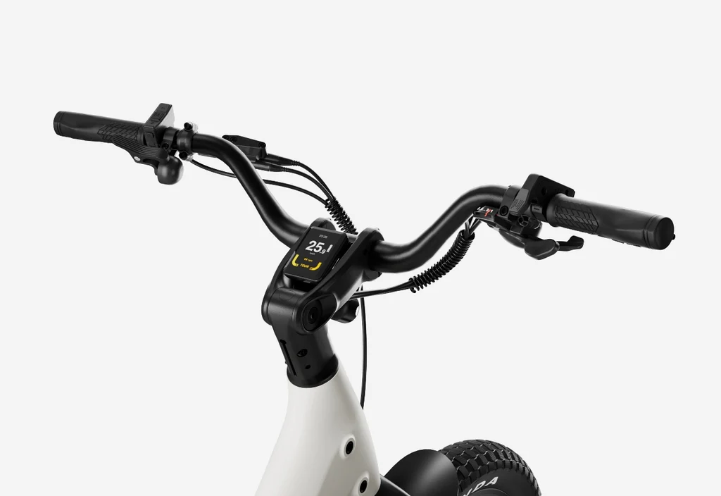 Close-up of Urtopia - Carbon Joy Ultra e-bike handlebars with a digital display showing speed and battery, brake levers, and a thick front tire, set against a plain background.