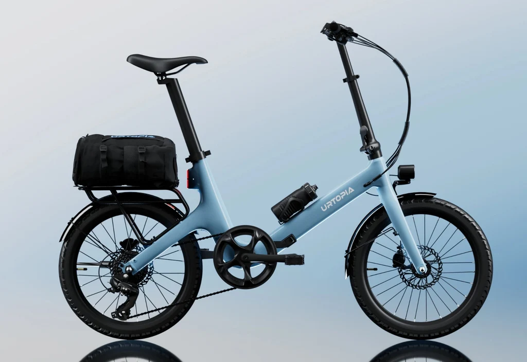 The Urtopia - Carbon Fold Step-Thru by Urtopia, a compact light blue e-bike with small wheels, a rear cargo bag, and a water bottle on the frame, is displayed against a gradient blue background.