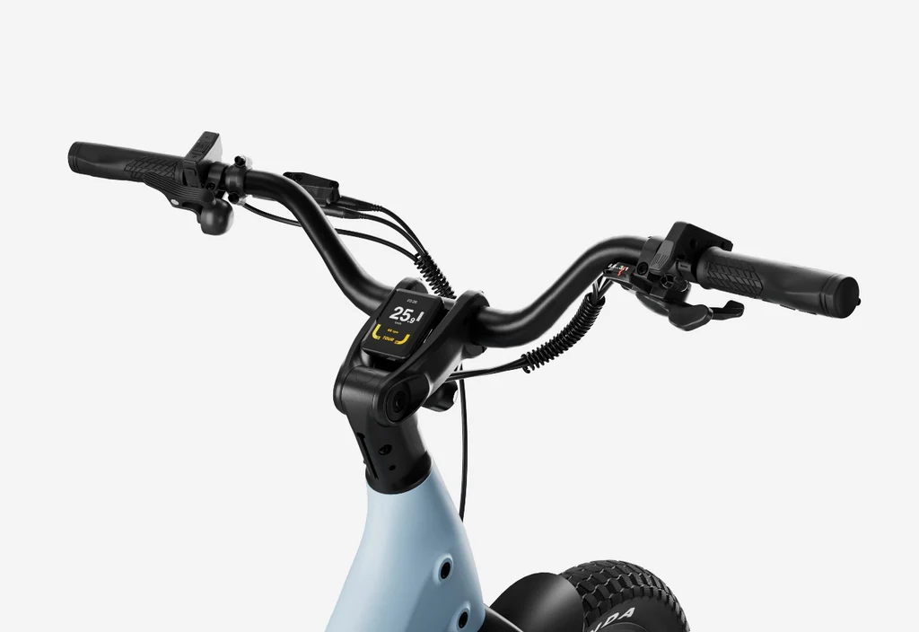 Close-up of Urtopia - Carbon Joy Ultra e-bike’s carbon fiber handlebars featuring a digital speed display, brake levers, and part of the front wheel, all set against a plain white background.