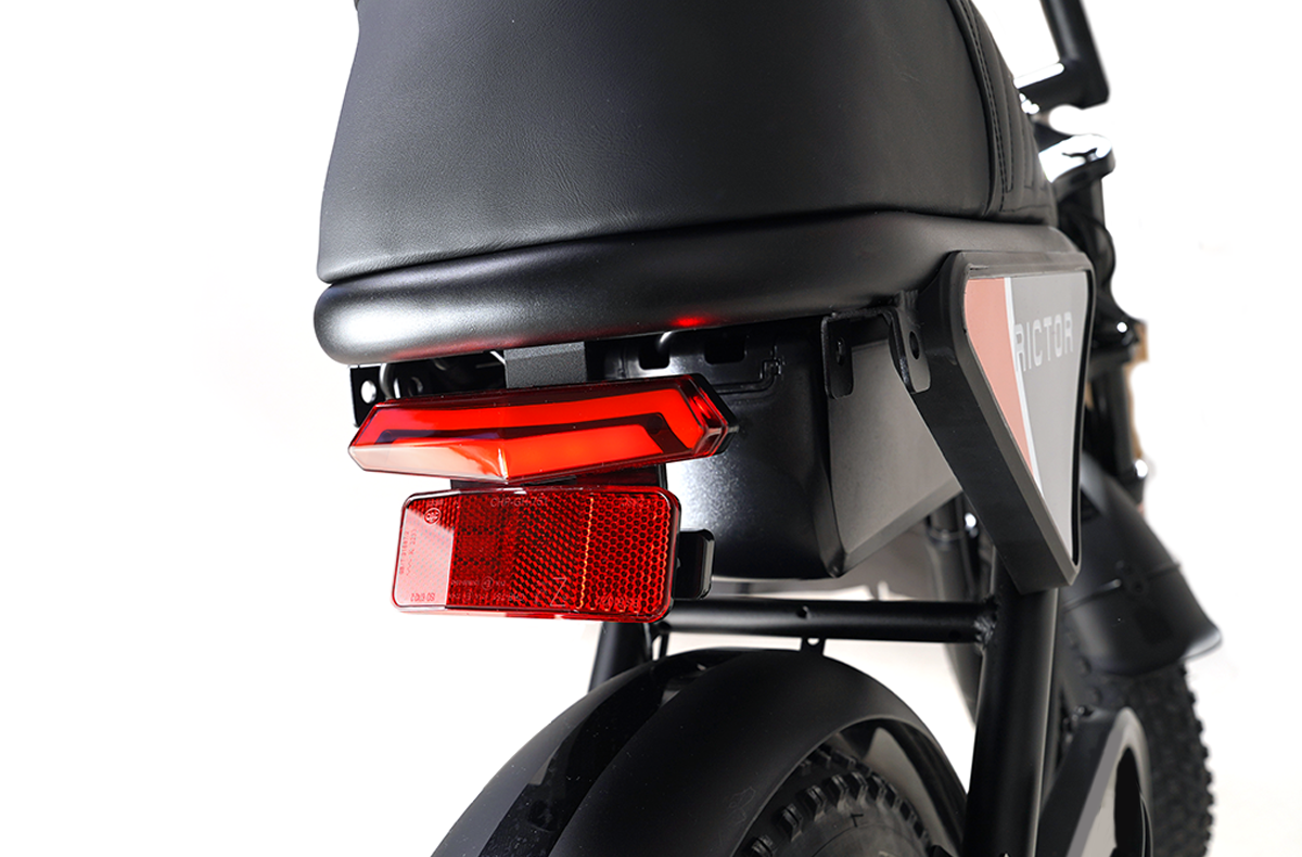 Close-up of the Rictor - Flexx by Rictor, highlighting its moped-style rear section with seat, tail light, red reflector, and part of the rear tire against a white background.