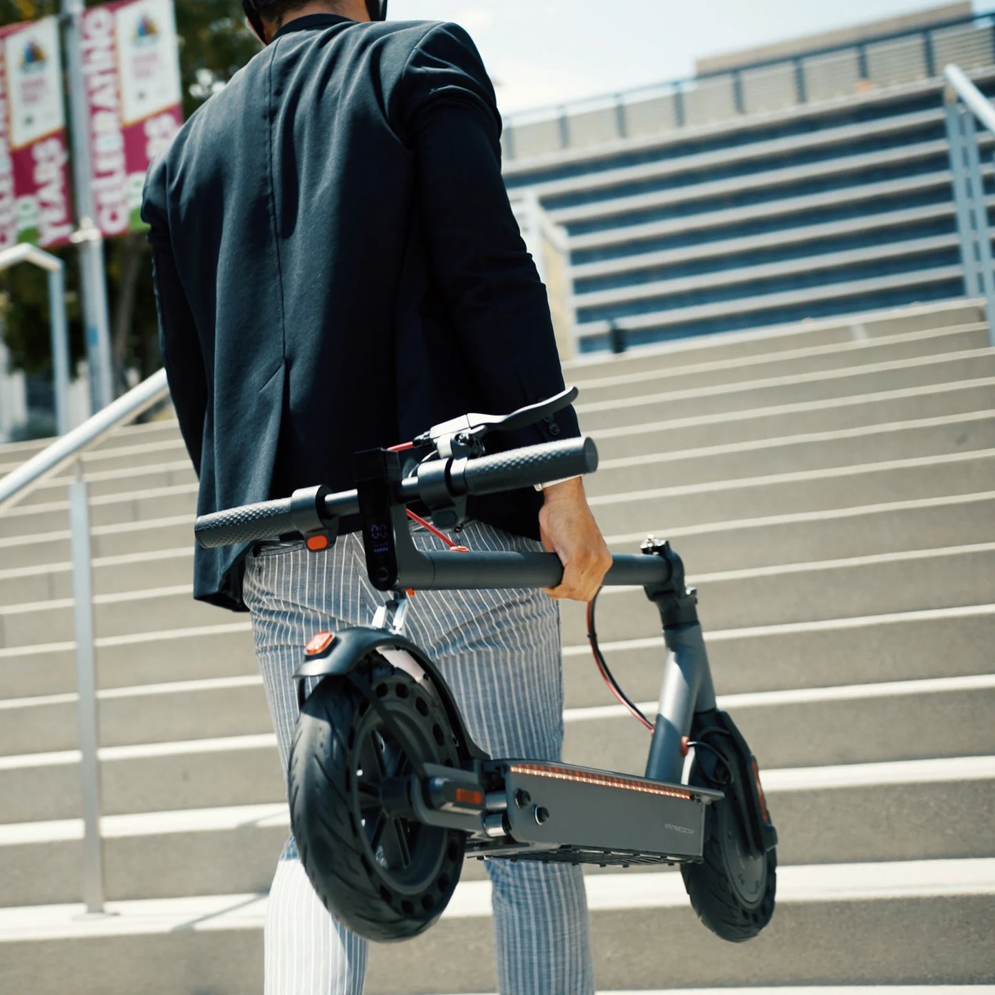 Person carrying a folded Hiboy - S2 Pro Electric Scooter up a set of outdoor stairs, wearing a black jacket and striped pants.