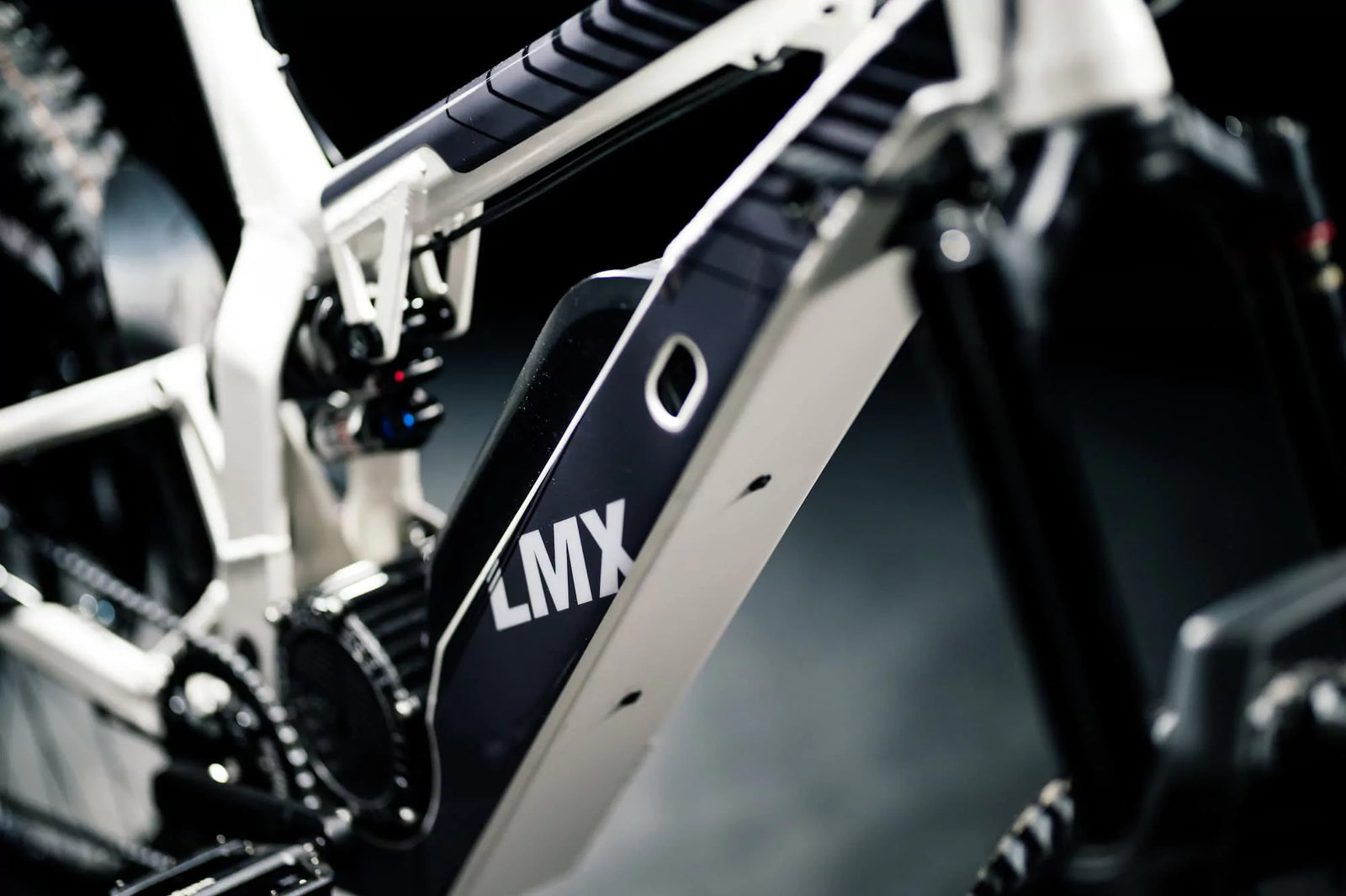 Close-up of a white LMX - 64 electric mountain bike frame, showcasing the central battery compartment, parts of the suspension system, and a robust brushless mid-mounted motor.