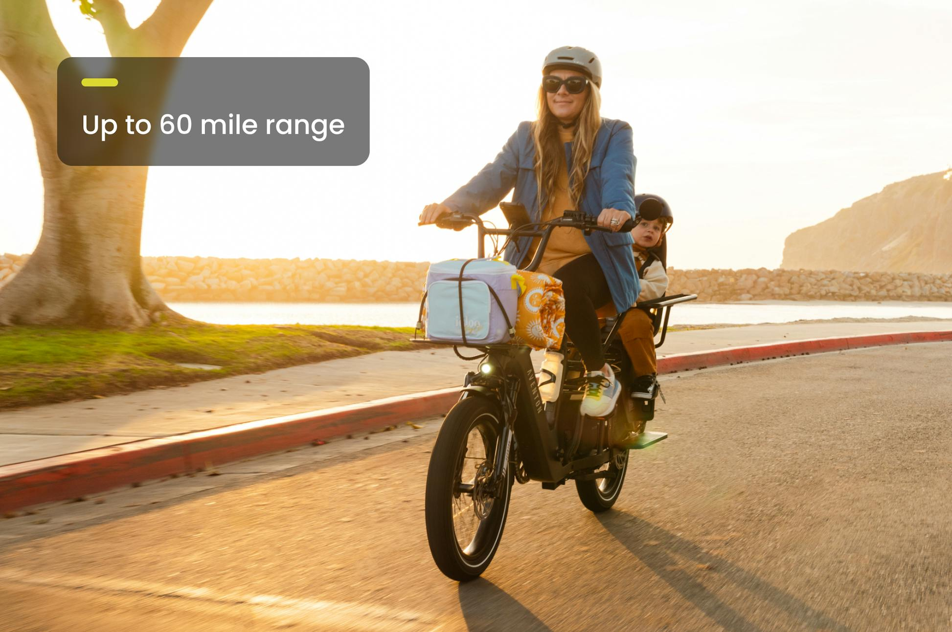 Two people ride the Aventon Abound LR cargo e-bike by the water on a sunny day; text reads, "Aventon Abound LR—Up to 60 mile range.