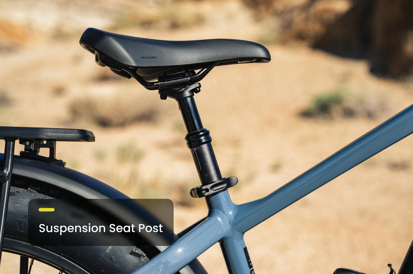 Close-up of the suspension seat post and saddle on a blue Aventon - Aventure M by Tampa Bay eBikes, highlighting its high-torque mid-drive fat tire design against a blurred outdoor backdrop.