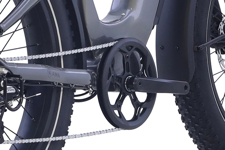 Close-up of the AIMA - Big Sur 2.0 electric bike drivetrain by AIMA, highlighting the chain, pedals, crankset, and a portion of the rear fat tire against a white background.
