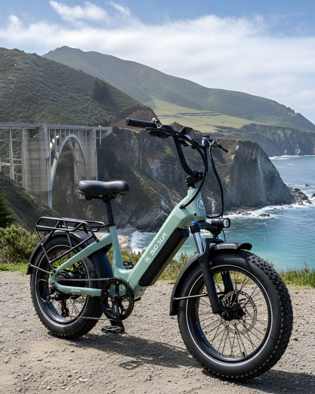 The AIMA - Big Sur Sport 2.0 e-bike by AIMA is parked on a coastal cliffside road with the Bixby Creek Bridge and ocean in the background.