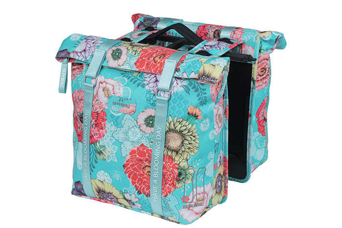 The Basil Bloom Field Double Pannier by Basil is a turquoise, waterproof bike bag made from recycled PET, featuring handles, straps, colorful flower designs, and the text "HAVE A BLOOMING DAY.