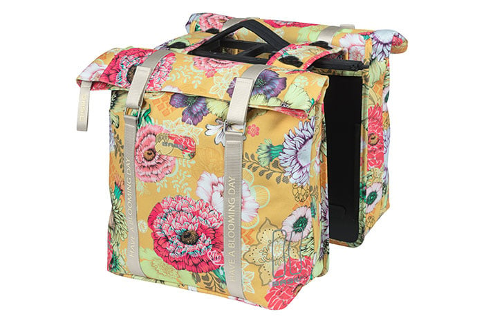 The Basil Bloom Field Double Pannier by Basil features a floral pattern with pink and purple flowers on a yellow background, grey straps, and is made from recycled PET. The bags are shown upright on a white surface.