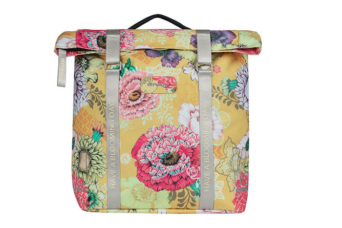 The Basil Bloom Field Double Pannier by Basil is a square, waterproof bike bag made from recycled PET, featuring a pink, red, and green floral print on yellow with gray "HAVE A BLOOMING DAY" straps—perfect for stylish rides.