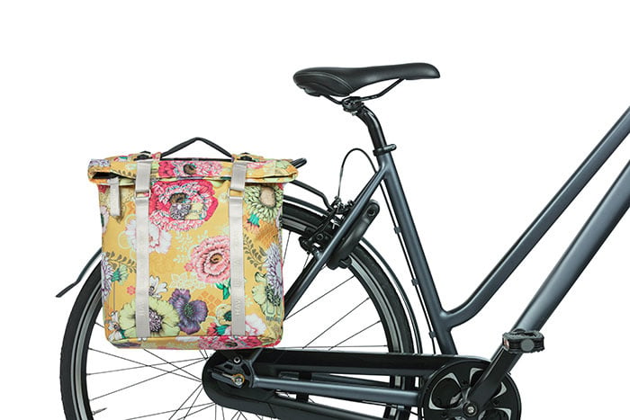 A bicycle with a Basil Bloom Field Double Pannier by Basil, featuring a yellow floral pattern, is attached to the rear rack and photographed against a white background.