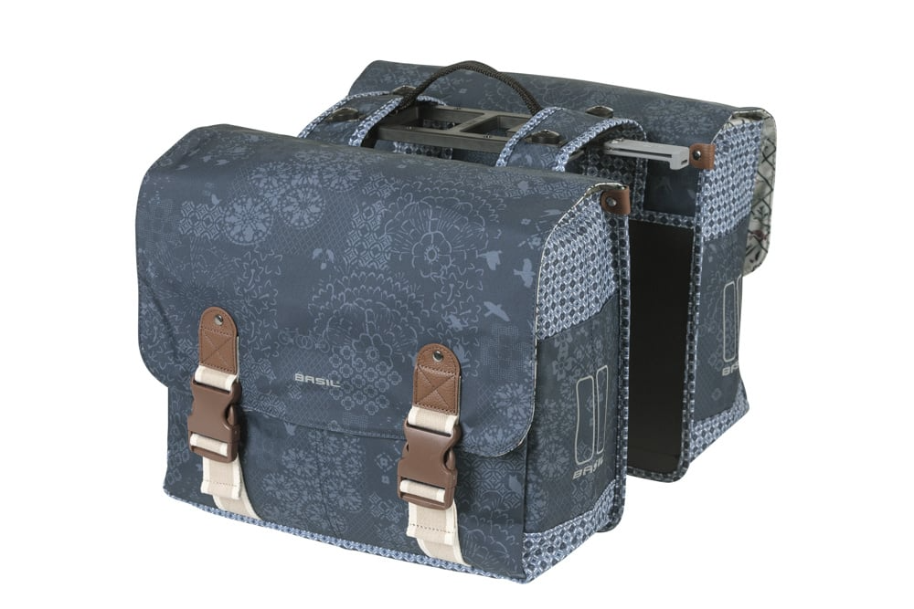 The Basil Boheme Double Pannier Bag by Basil is a blue patterned pair of bicycle pannier bags with brown buckle straps, joined by a central handle and top mounting hardware.