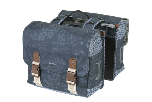 The Basil Boheme Double Pannier Bag by Basil is a blue patterned pair of bicycle pannier bags with brown buckle straps, joined by a central handle and top mounting hardware.