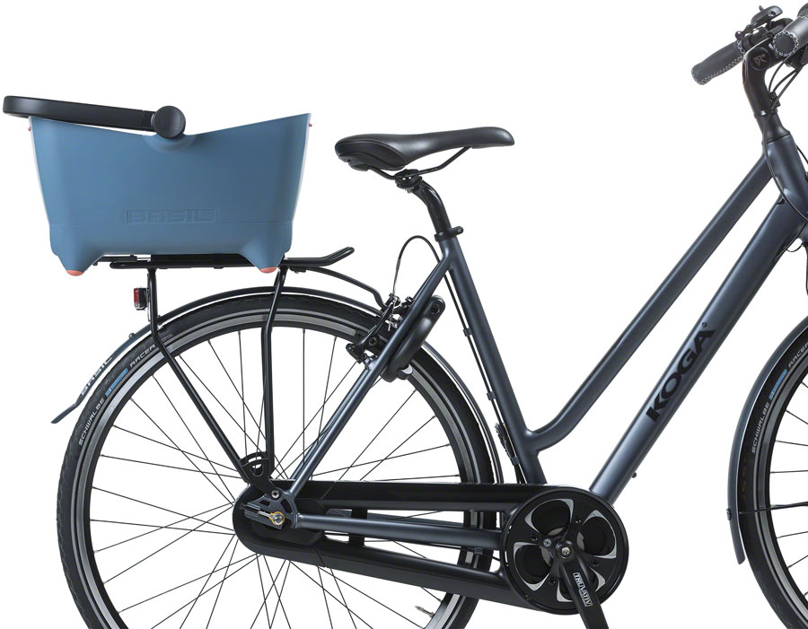 The Basil Buddy Dog Basket MIK by Basil—a blue, MIK-compatible pet carrier—is mounted on the rear rack of a black bicycle, making it an ideal eBike accessory.