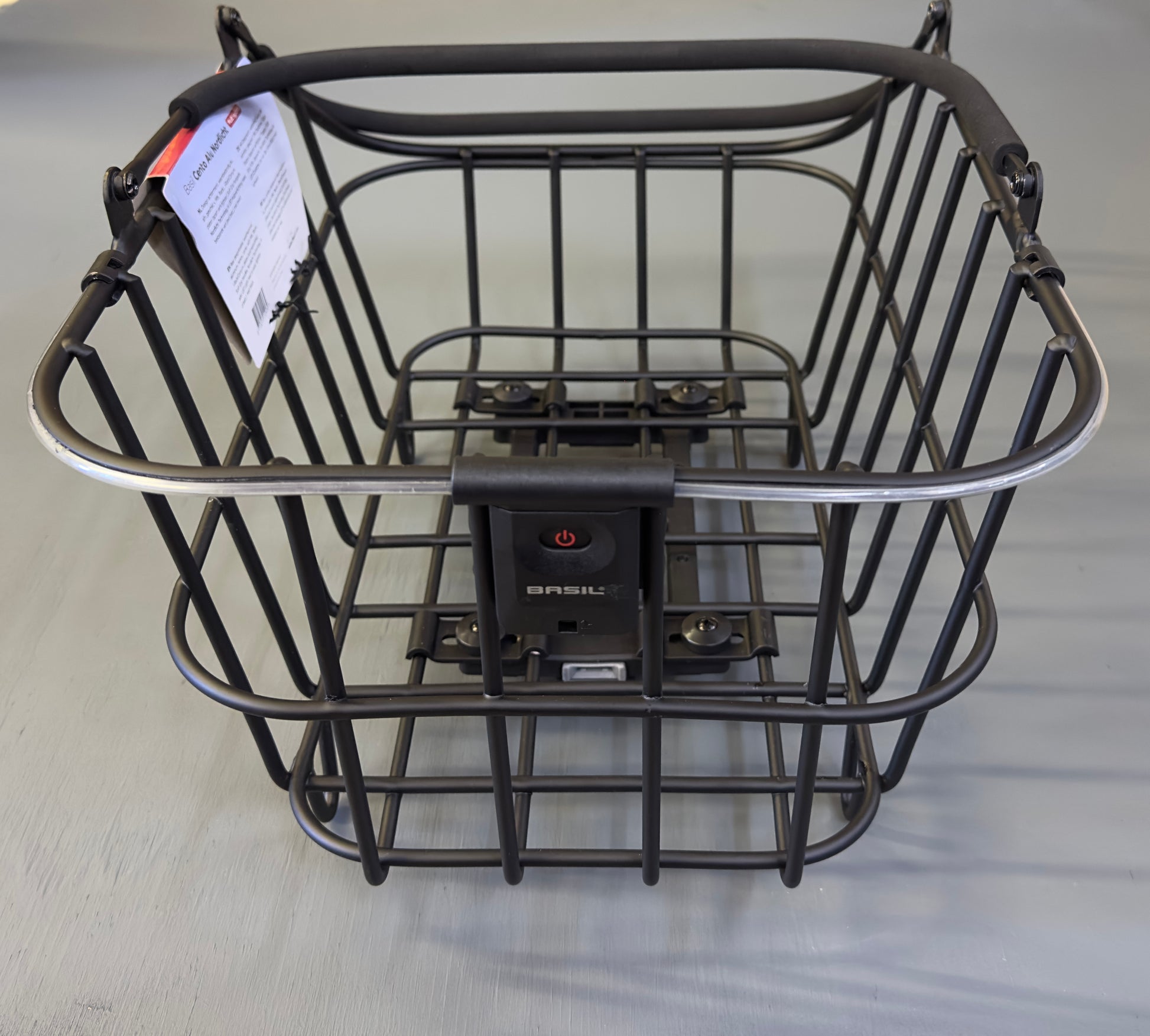The Basil Cento MIK rear basket in black, complete with mounting hardware and label, is shown on a light gray surface.