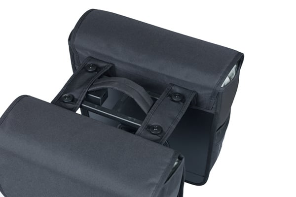 Close-up of the Basil Go MIK Double Pannier Bag by Basil in black, attached to a bicycle rear rack, featuring fabric flaps and button fasteners.