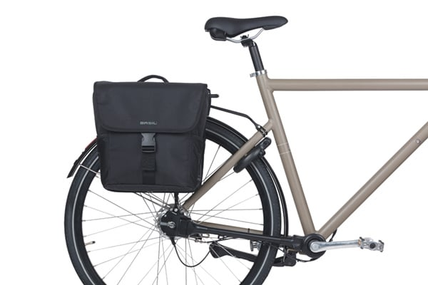 A Basil Go MIK Double Pannier Bag by Basil is attached to the rear rack of a beige bicycle, set against a white background.