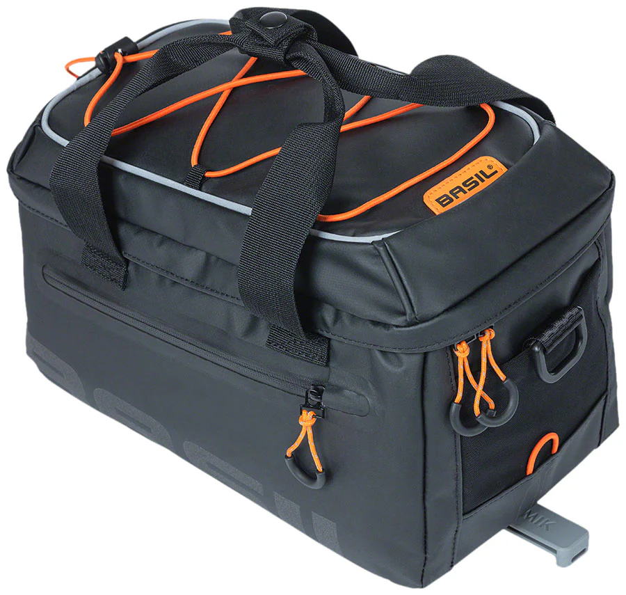 A black and gray Basil Miles MIK Orange bike bag with orange accents, multiple zippers, and handles on top. The bag has a rectangular shape and attached mounting hardware at the bottom.