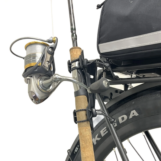 A Bikase Fishing Rod Holder secures a spinning rod and reel to the rear rack of a bike with a Kenda tire and a black bag.