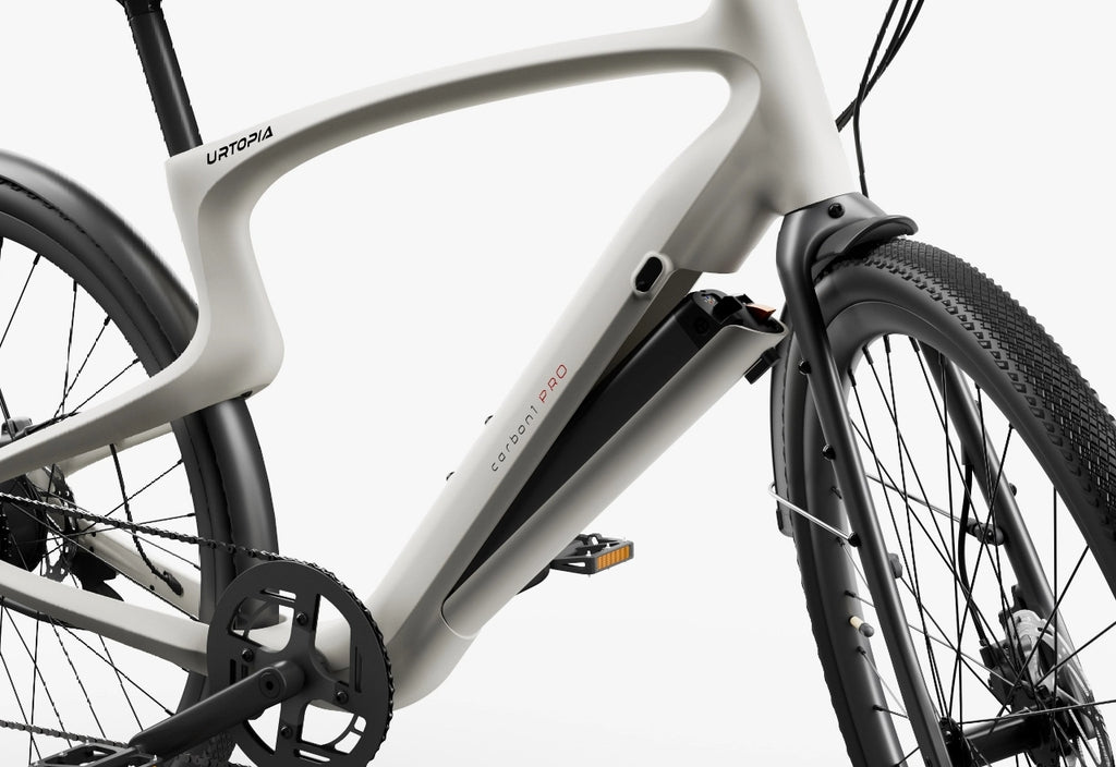 Close-up of the Urtopia - Carbon Classic by Urtopia, a lightweight electric bike in a light color, highlighting its battery compartment, front wheel, pedal, and part of the drivetrain.