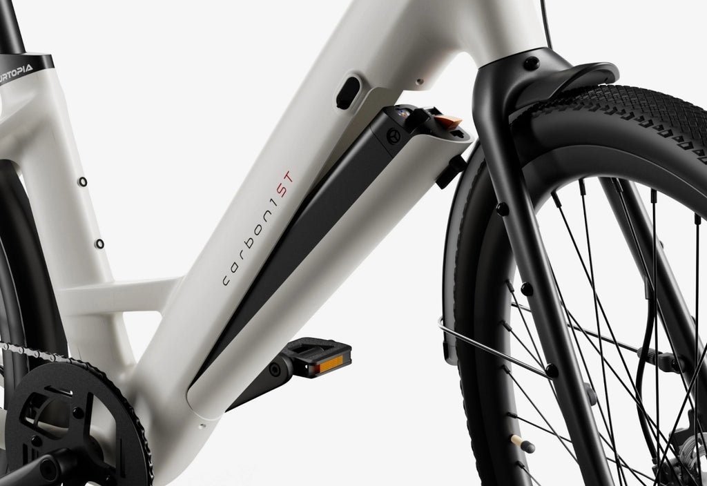 Close-up of the Urtopia - Carbon Classic Step-Thru by Urtopia, showcasing its lightweight carbon frame, removable Samsung battery compartment, pedal, and front wheel labeled "carbon 15T.