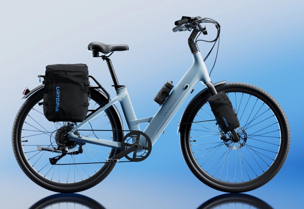The Urtopia - Carbon Classic Step-Thru by Urtopia, a light blue carbon eBike with upright handlebars, wide tires, front and rear gear bags, and a removable Samsung battery, is shown on a gradient blue background.