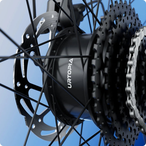 Close-up of the Urtopia - Carbon Classic Step-Thru’s lightweight carbon wheel hub, showing "URTOPIA" branding, cassette, gear cogs, disc brake, and spokes set against a gradient blue background.