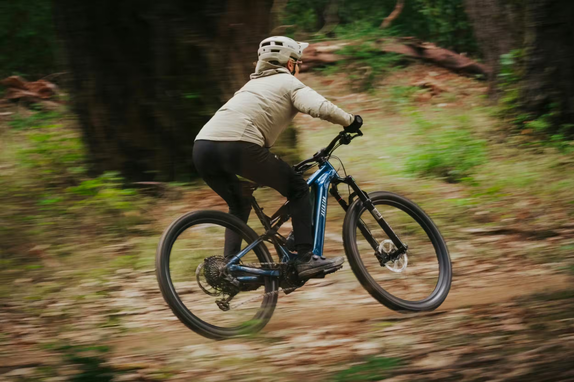 Wearing a helmet and jacket, a rider speeds through the woods on the Aventon Current ADV electric mountain bike by Aventon.